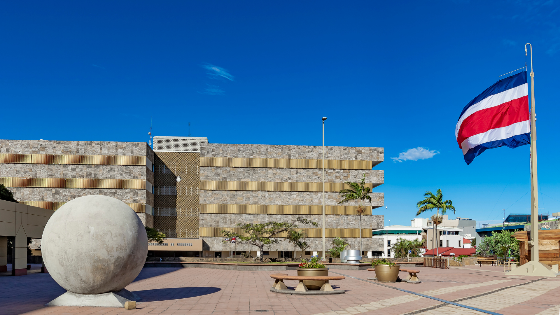 La imagen muestra el edificio del Poder Judicial de Costa Rica, una bandera de Costa Rica y una de las esferas de piedra de Costa Rica.